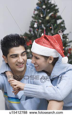 Stock Photo - Young woman wearing a Santa hat and embracing a young man. Fotosearch