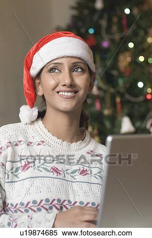 Stock Photography - Young woman wearing a Santa hat and using a laptop. Fotosearch