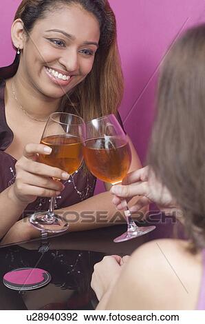 Stock Image - Young woman with another woman toasting with wine glasses. Fotosearch