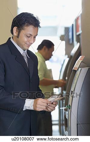 Businessman using an ATM at an airport View Large Photo Image Stock Photo - Businessman using an ATM at an airport. Fotosearch