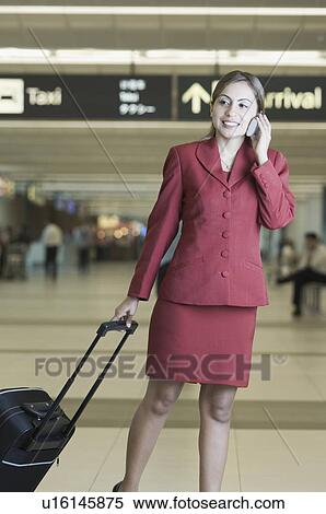 Businesswoman pulling her luggage while talking on a mobile phone View Large Photo Image Stock Photography - Businesswoman pulling her luggage while talking on a mobile phone. Fotosearch