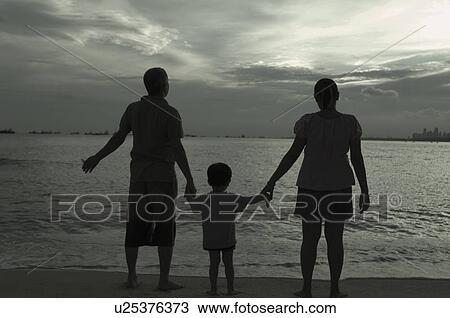 Stock Image - Rear view of a mid adult couple standing on the beach with their son and holding hands. Fotosearch