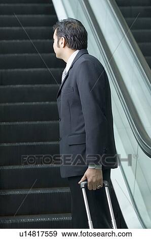 Side profile of a businessman standing near an escalator View Large Photo Image Stock Photo - Side profile of a businessman standing near an escalator. Fotosearch