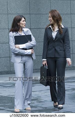 Two businesswomen talking to each other and smiling View Large Photo Image Stock Image - Two businesswomen talking to each other and smiling. Fotosearch