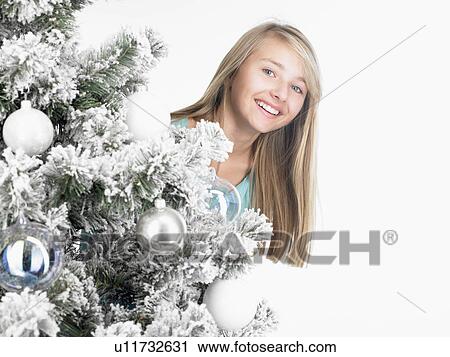 Stock Image - girl standing behind a fir-tree, smiling. Fotosearch