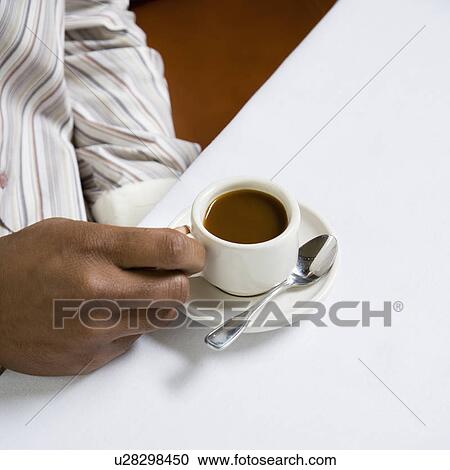 Stock Image - African American male hand holding handle of expresso cup.. Fotosearch