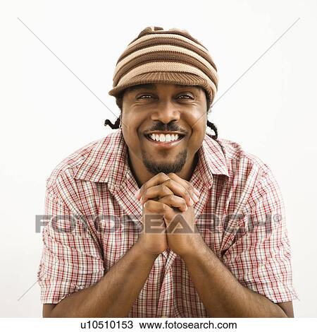 Stock Image - African-American mid-adult man wearing hat and smiling at viewer with hands together.. Fotosearch