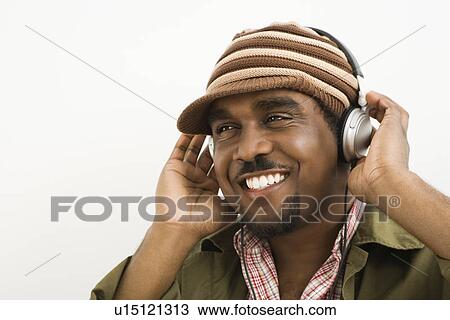 Stock Image - African-American mid-adult man wearing knit hat and listening to headphones smiling.. Fotosearch
