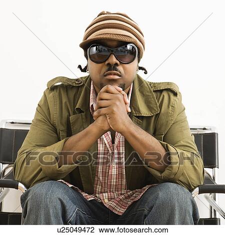 Stock Image - African-American mid-adult man wearing hat and sunglasses and looking at viewer.. Fotosearch