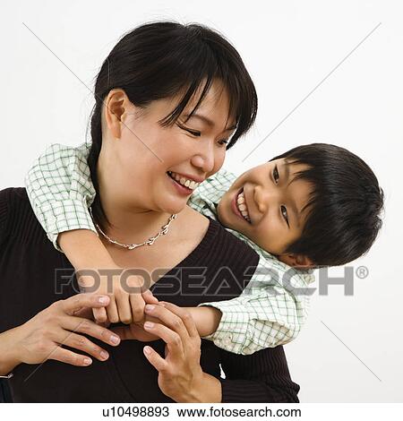 Asian mother with young son hugging her from behind smiling. View Large Photo Image Stock Image - Asian mother with young son hugging her from behind smiling.. Fotosearch