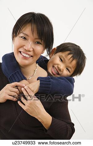 Stock Image - Asian mother with young son hugging her from behind smiling.. Fotosearch
