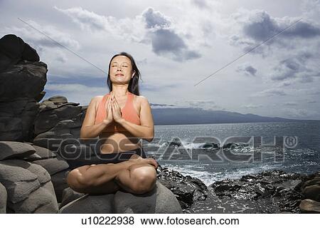Asian woman sitting on rock by ocean in lotus pose with eyes closed in Maui, Hawaii View Large Photo Image Stock Photo - Asian woman sitting on rock by ocean in lotus pose with eyes closed in Maui, Hawaii. Fotosearch