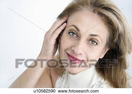 Stock Image - Attractive woman with hand to face smiling at viewer. Fotosearch
