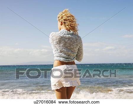 Picture - Back view of young blond woman standing at water's edge on Maui, Hawaii beach gazing at the ocean.. Fotosearch