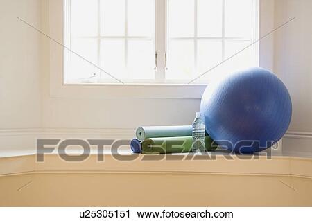 Stock Image - Balance ball exercise mats and bottled water at gym by window. Fotosearch
