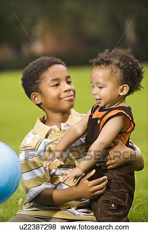 Stock Photo - Big brother and little brother playing with ball in park. Fotosearch