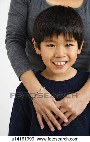 Boy smiling with mother standing behind with arms around him View Large Photo Image Stock Photo - Boy smiling with mother standing behind with arms around him. Fotosearch
