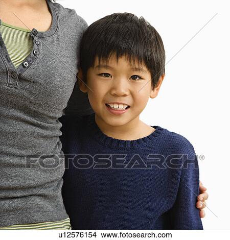 Picture - Boy standing smiling with mother standing next to him with arm around him.. Fotosearch