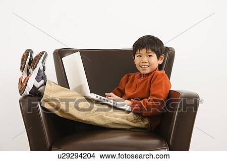 Boy with laptop computer sitting in chair smiling View Large Photo Image Picture - Boy with laptop computer sitting in chair smiling. Fotosearch