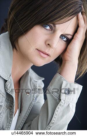 Picture - Brunette woman looking at viewer resting head on hand. Fotosearch