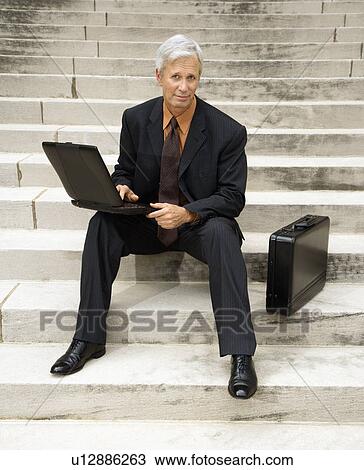 Businessman sitting on steps outdoors with laptop and briefcase View Large Photo Image Stock Image - Businessman sitting on steps outdoors with laptop and briefcase. Fotosearch