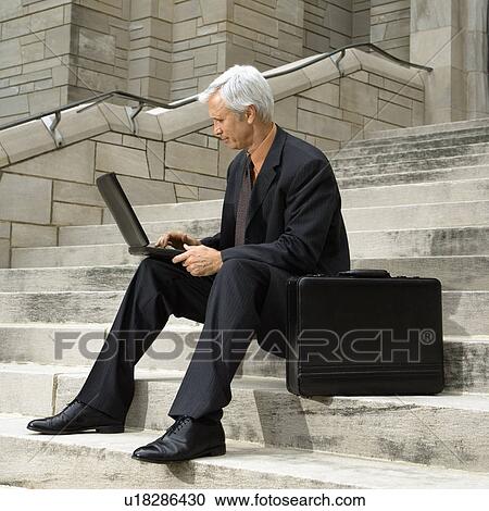 Businessman sitting on steps outdoors with laptop and briefcase View Large Photo Image Stock Image - Businessman sitting on steps outdoors with laptop and briefcase. Fotosearch