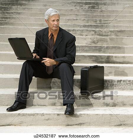 Businessman sitting on steps outdoors with laptop and briefcase View Large Photo Image Stock Photo - Businessman sitting on steps outdoors with laptop and briefcase. Fotosearch