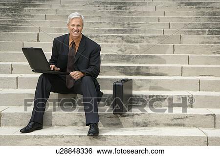 Stock Photograph - Businessman sitting on steps outdoors with laptop and briefcase. Fotosearch