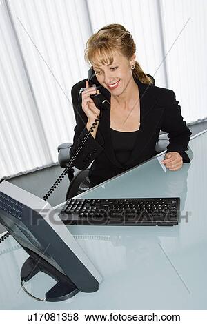 Stock Photo - Businesswoman at computer desk on telephone. Fotosearch