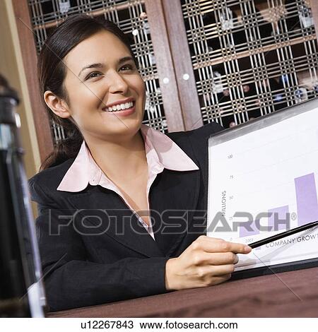 Stock Image - Businesswoman smiling and pointing to bar graph.. Fotosearch