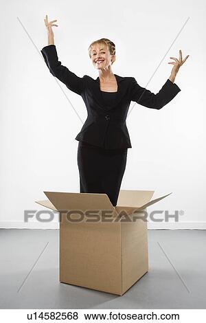 Stock Photo - Businesswoman standing in cardboard box gesturing above head and smiling at viewer. Fotosearch
