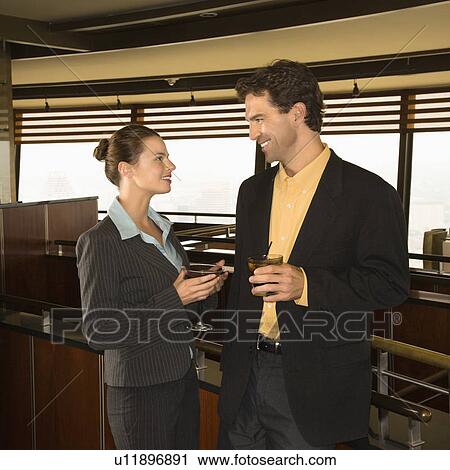 Stock Image - Caucasian business man and woman conversiting with alcoholic beverages.. Fotosearch