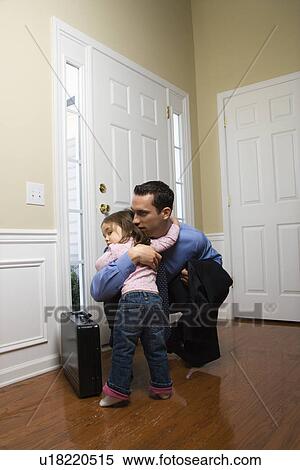 Stock Photography - Caucasian businessman at door with briefcase hugging daughter.. Fotosearch