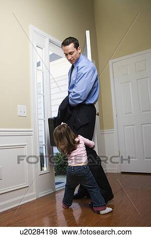 Stock Photo - Caucasian businessman at open door with briefcase with daughter tugging on his leg.. Fotosearch
