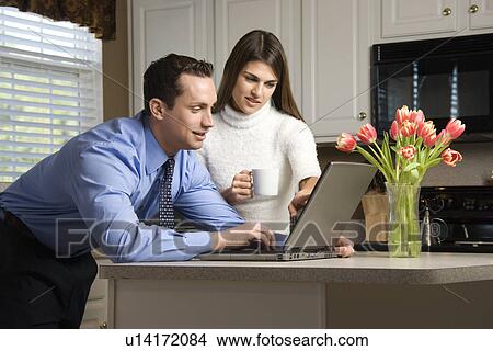 Caucasian couple in kitchen with coffee looking at laptop computer. View Large Photo Image Picture - Caucasian couple in kitchen with coffee looking at laptop computer.. Fotosearch