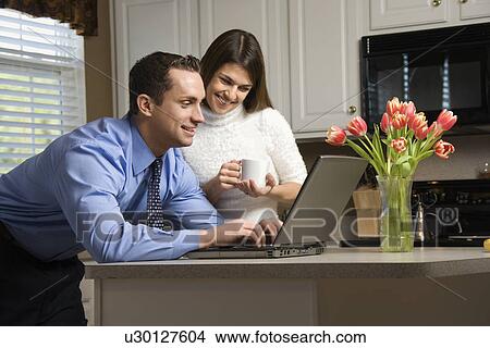 Picture - Caucasian couple in kitchen with coffee looking at laptop computer.. Fotosearch