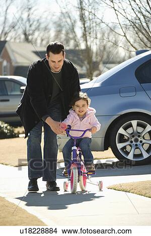 Caucasian father helping daughter ride bicycle. View Large Photo Image Picture - Caucasian father helping daughter ride bicycle.. Fotosearch