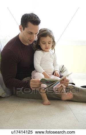 Stock Photography - Caucasian father reading book to girl on lap sitting on floor.. Fotosearch