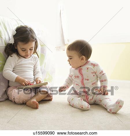 Stock Image - Caucasian girl children sitting on bedroom floor looking at book.. Fotosearch