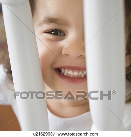Stock Photo - Caucasian girl toddler smiling and peering between railing.. Fotosearch