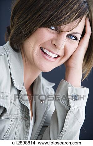 Picture - Caucasian mid adult brunette woman smiling at viewer resting head on hand.. Fotosearch