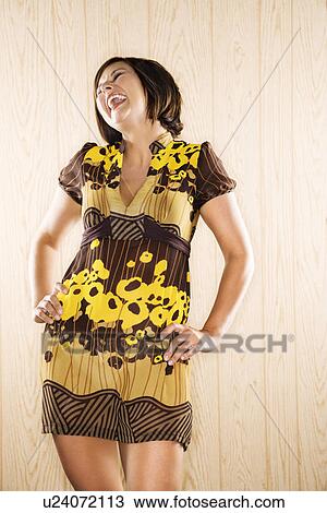 Stock Image - Caucasian mid adult brunette woman standing with hands on hips laughing.. Fotosearch