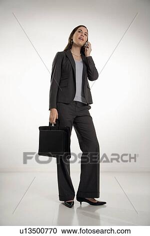 Stock Image - Caucasian mid adult professional business woman holding briefcase, talking on cell phone and smiling.. Fotosearch