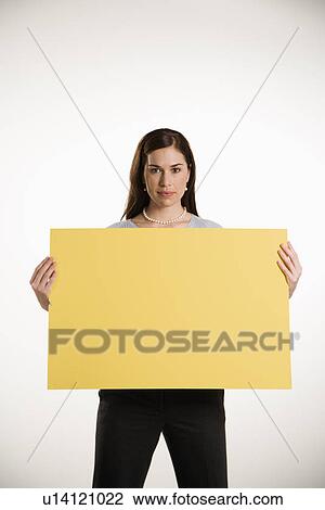 Stock Image - Caucasian mid adult professional business woman standing holding up blank yellow sign.. Fotosearch