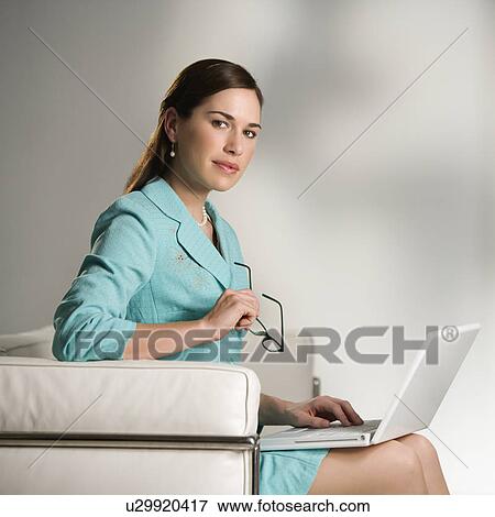 Caucasian mid adult professional business woman sitting in modern office working on laptop computer holding eyeglasses and looking at viewer. View Large Photo Image Stock Photo - Caucasian mid adult professional business woman sitting in modern office working on laptop computer holding eyeglasses and looking at viewer.. Fotosearch