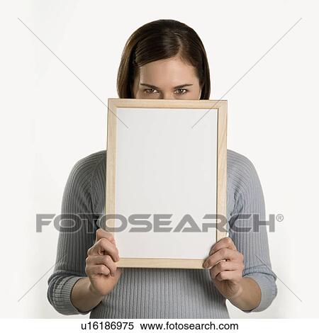 Stock Photography - Caucasian mid adult professional business woman peeking over top of blank dry erase board in front of her face.. Fotosearch