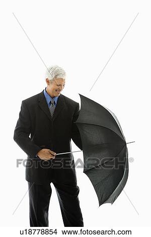 Picture - Caucasian middle aged businessman closing umbrella.. Fotosearch