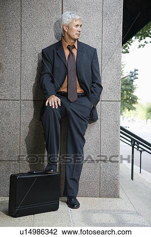 Caucasian middle aged businessman leaning on wall outdoors with foot on briefcase. View Large Photo Image Stock Image - Caucasian middle aged businessman leaning on wall outdoors with foot on briefcase.. Fotosearch