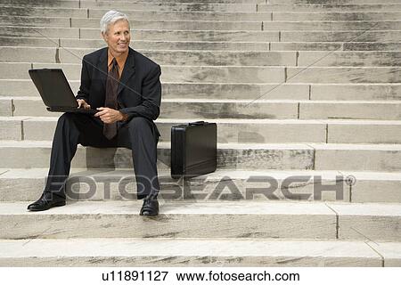 Caucasian middle aged businessman sitting on steps outdoors with laptop and briefcase. View Large Photo Image Stock Photo - Caucasian middle aged businessman sitting on steps outdoors with laptop and briefcase.. Fotosearch