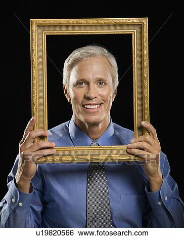 Stock Photograph - Caucasian middle aged businessman smiling through empty picture frame in front of face.. Fotosearch